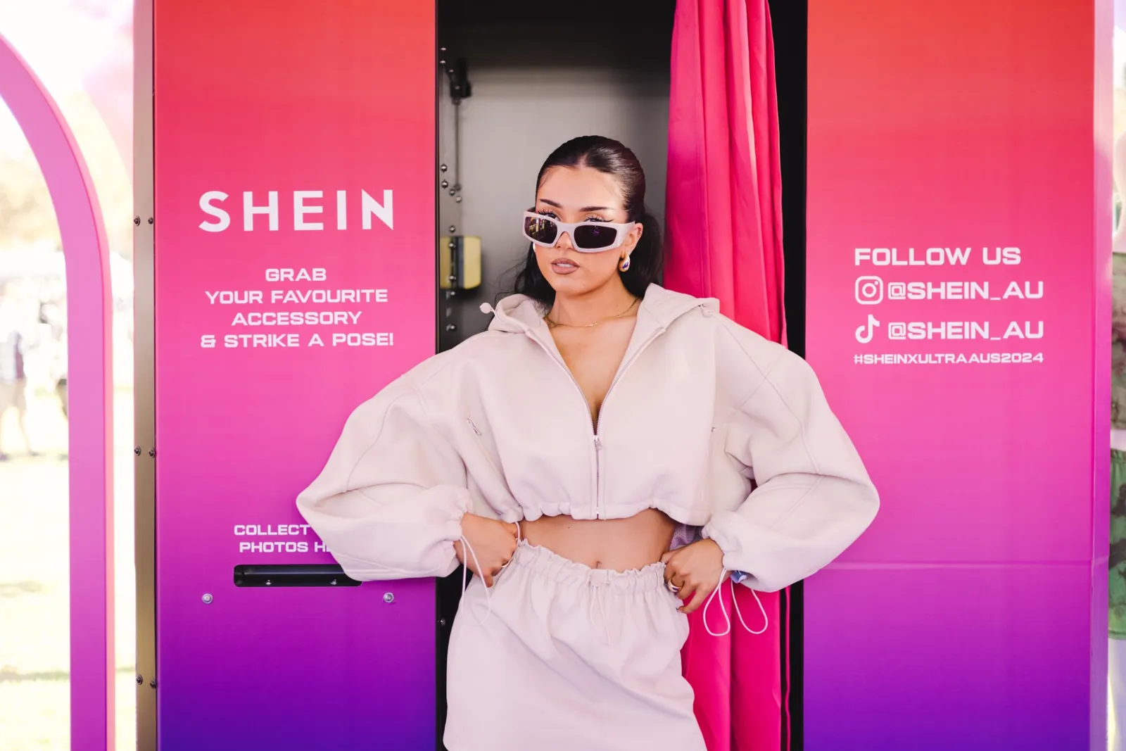 A guest in sunglasses posing at a pink SHEIN-branded photo booth at a festival