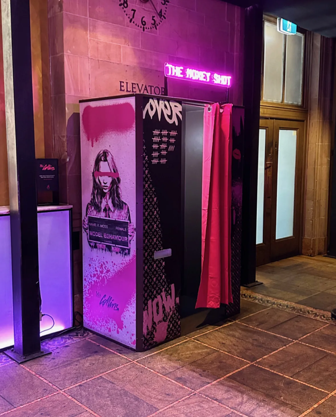 A street-art wrapped photo booth under a pink The Money Shot neon sign at Ms Collins